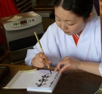 Japanese woman in a kimono at Heian Jingu Shrine writing with a brush